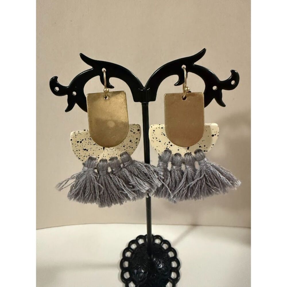 Brass-colored arch, a speckled white clay piece, and gray thread tassels.